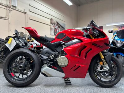 Red Ducati sport motorcycle side view inside a used bike showroom with other motorcycles behind.