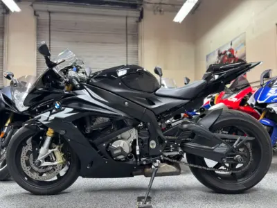 Black BMW S1000RR sport motorcycle parked indoors with other bikes in background.