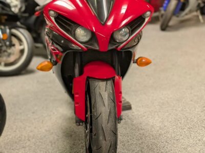 Front‑facing red sport motorcycle with twin headlights and visible front tire on display inside a showroom.