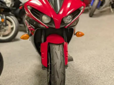 Front‑facing red sport motorcycle with twin headlights and visible front tire on display inside a showroom.